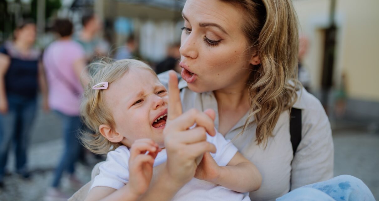 Mother scolding her little daughter in street. Child is crying and woman is shaking finger because